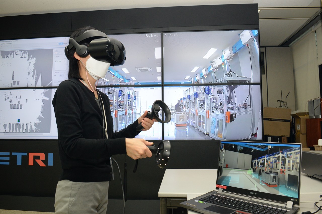 ETRI 연구진이 현장 스마트공장과 로봇 상황과 연동되는 VR 기기로 현장을 점검하고 있다.